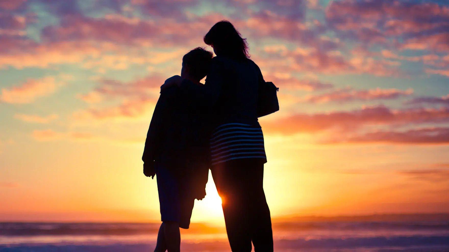 Dos personas paradas en la playa frente al atardecer